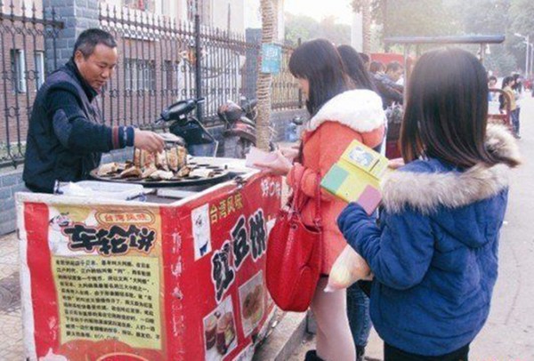 刘卫东（左）在湘潭大学的流动小摊点上卖红豆饼来供养妻子李时华读书。（网络图片）