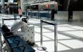 5月13日，一名身穿保护衣的男子在美国肯尼迪机场趴在行李箱上睡觉。（图片来源：JOHANNES EISELE/AFP via Getty Images）