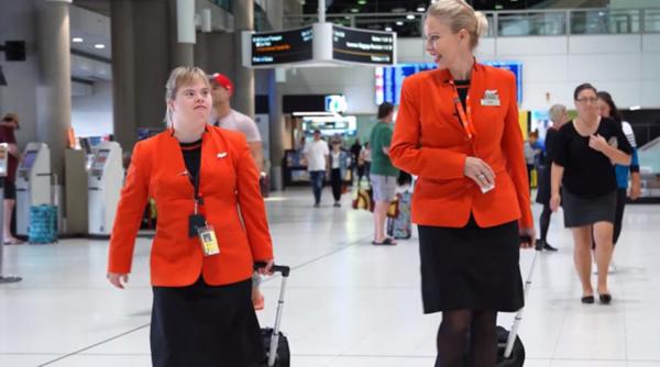 Knoll穿上红色的空姐制服，拖着行李箱，昂首挺胸地走在机场大厅内。(视频截图)