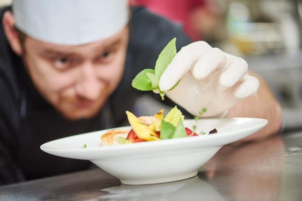 一名男性厨师正在餐厅厨房装饰沙拉盘。（123RF）