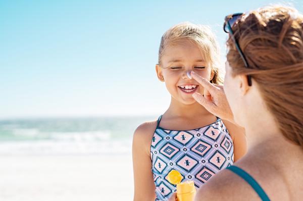 沙滩上，一位母亲给女儿涂防晒霜。(123RF)