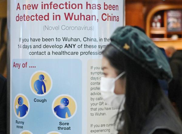 2020年1月28日，伦敦希思罗机场，一名戴着口罩的女士走过写有提醒武汉肺炎疫情的标语牌。（AFP via Getty Images）