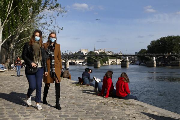 戴着口罩的行人在巴黎塞纳河边路过，背后是艺术桥和新桥。（Chesnot/Getty Images）