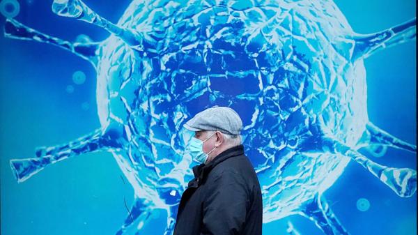 英国一名戴口罩男子在奥尔德姆（Oldham）地区科学中心COVID-19病毒图片前经过。（Christopher Furlong/Getty Images）