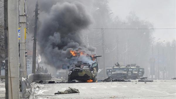 2月27日，在乌克兰第二大城市哈尔科夫，俄军在与乌克兰武装部队的战斗中，一辆俄罗斯装甲运兵车 (APC) 在身份不明的士兵尸体旁燃烧。（SERGEY BOBOK/AFP via Getty Images)