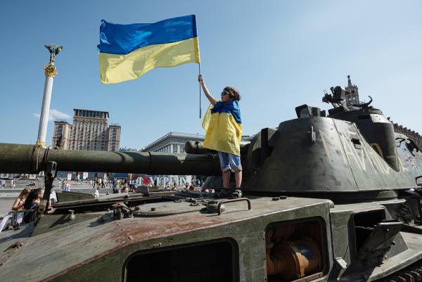 图为2022年8月21日，在乌克兰首都基辅市中心，一个小男孩手持并身裹一面乌克兰国旗站在一辆被缴获的俄罗斯军车上。（Alexey Furman/Getty Images）