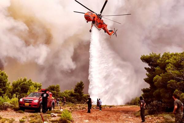 图为一架消防直升机正在雅典附近的村庄灭火。（Getty Images）