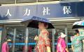 几位手持雨伞的老年妇女走过人力资源与社会保障局办公室的入口。（CHENG XIN/GETTY IMAGES）