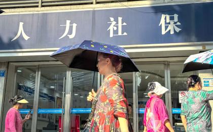 几位手持雨伞的老年妇女走过人力资源与社会保障局办公室的入口。（CHENG XIN/GETTY IMAGES）