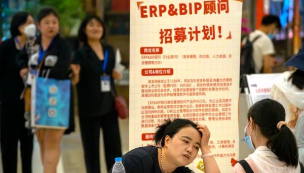 资料照片:2023年6月9日,一名招聘人员在北京一家购物中心招聘会的展位上与申请人交谈。(图片来源:网络截图)
