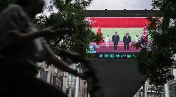 2026年6月8日，一名女子骑车经过北京一家购物中心外的大萤幕，萤幕上正在播放中共党魁习近平与北韩领导人金正恩在北韩会晤的新闻报道。(图片来源：Pedro PARDO/AFP via Getty Images)