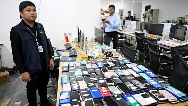 2026年3月11日，柬埔寨金边警方在前一晚突袭行动后，一名警员在一处网络诈骗指挥中心旁站岗，身边摆放着智能手机及其他查获的设备。（图片来源：TANG CHHIN Sothy/AFP via Getty Images）