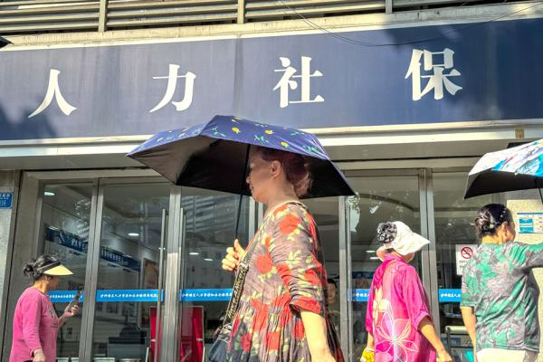 几位手持雨伞的老年妇女走过人力资源与社会保障局办公室的入口。(CHENG XIN/GETTY IMAGES)