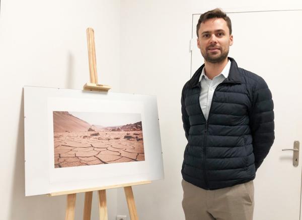 摄影师谢勒(Savin Scherer)当日在ASIEMUT联合会画廊内,左边是其作品《火焰山》。(摄影:程茗芝/看中国)